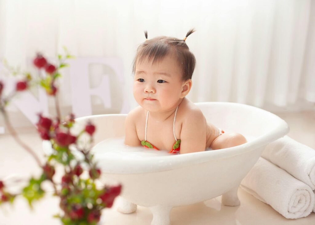 Sweet Asian little girl in swimwear sitting in small bathtub and bathing at home